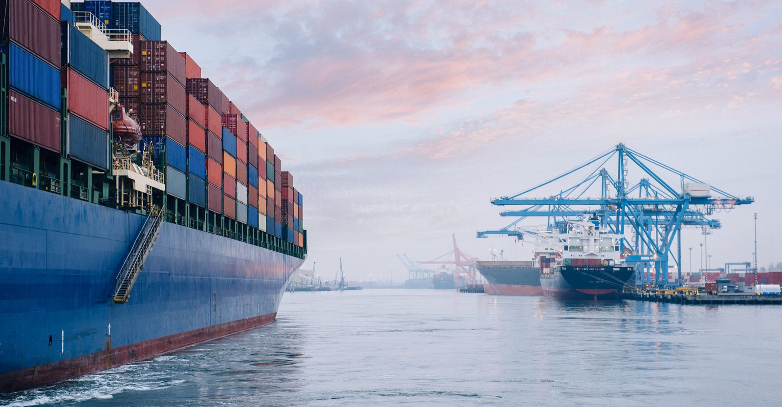 Container ship arriving at a port with cranes at sunrise